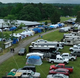 Sovereign Health Summit event grounds in Harmony, North Carolina, with RVs, trucks, and vendor tents lining a gravel road beside the large barn, surrounded by trees and open fields.