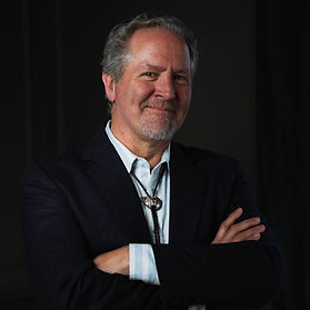 Dr. Wil Spencer standing with arms crossed in a dark blazer.