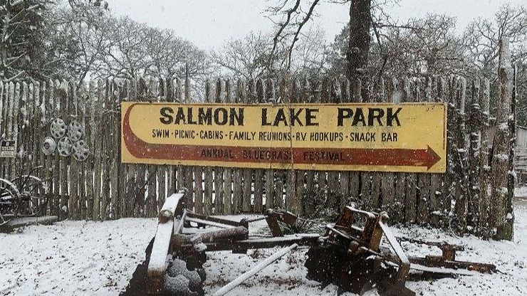 Winter scene of Sign that reads "Salmon Lake Park Swim Picnic Cabins Family Reunions RV Hookups Snack Bar Annual Bluegrass Festival"