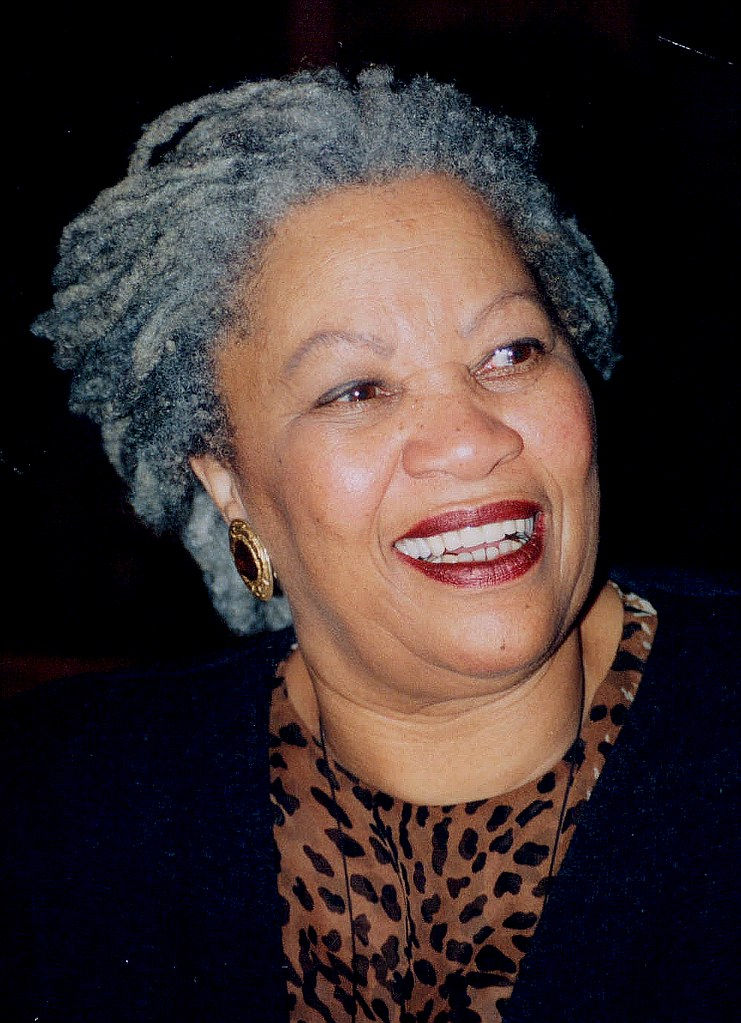 Photo of Toni Morrison with her grey locs pulled back, looking off to the side and smiling by John Mathew Smith & www.celebrity-photos.com from Laurel Maryland, USA, CC BY-SA 2.0 <https://creativecommons.org/licenses/by-sa/2.0>, via Wikimedia Commons