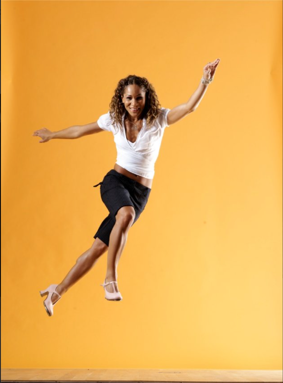 Ayodele Casel dancing and flying through the air in front of a rich yellow background