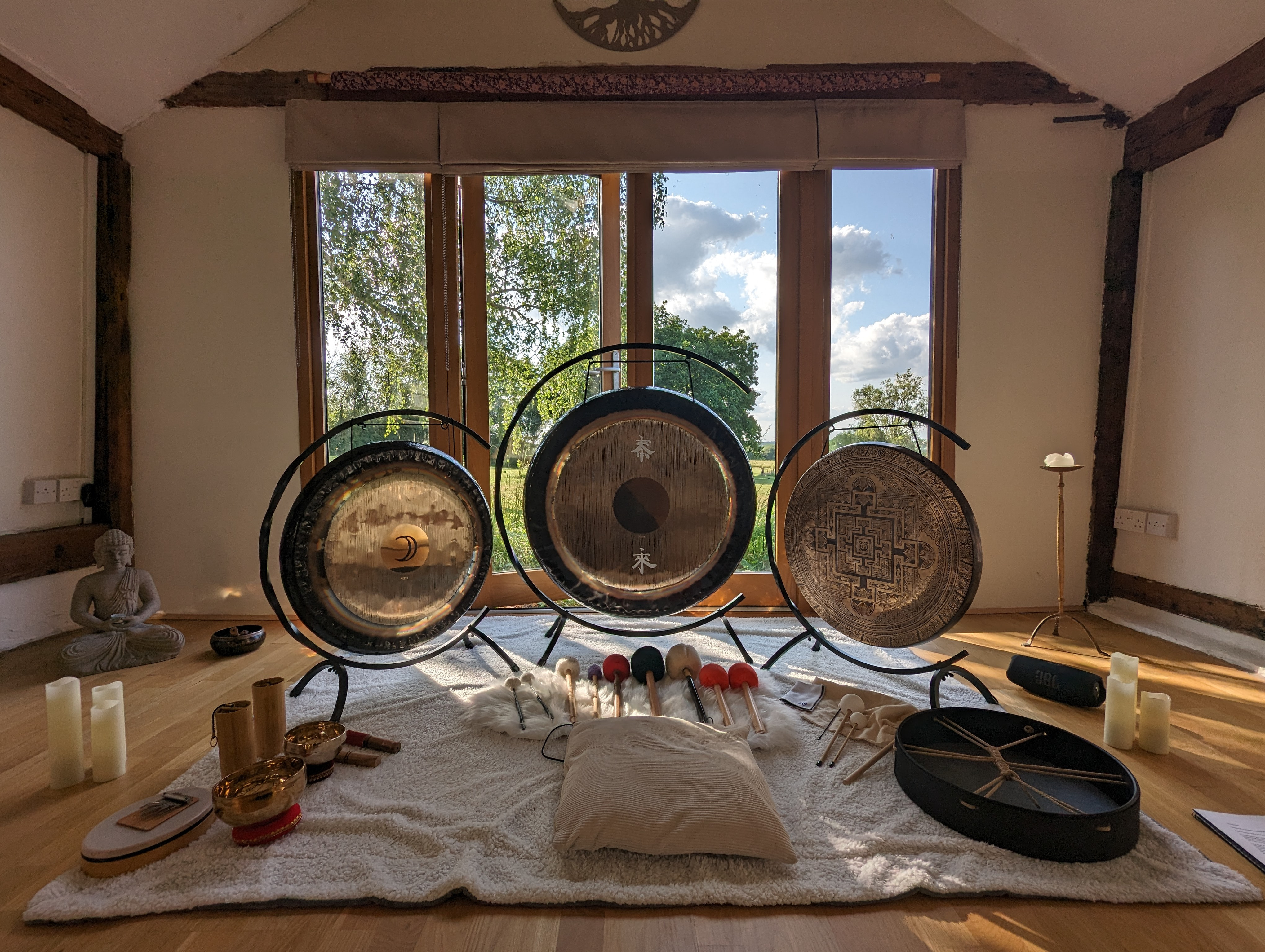 Sound healing room with gongs, mallets, candles, and a cushion by a window