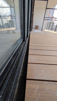 דק במבוק סינטטי מותקן בצמוד לדלת הזזה מזכוכית במרפסת בבניין משופץ ברחוב פרופסור שור בתל אביב, עבודה של צוות המקצוענים בהתקנת דק עץ של WOOD PRO