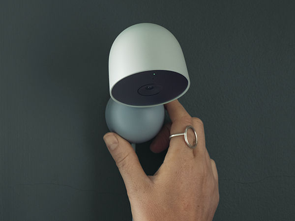 Miniatura: A hand adjusts a white camera on a gray wall for optimal monitoring.