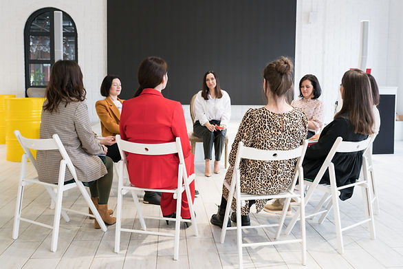 women-sitting-on-chairs-in-circle-and-talking-to-psychologist-coach-and-audience-discuss-t