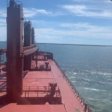 Açık denizde seyreden büyük bir kargo gemisi, yakınında küçük bir tekne, parlak gökyüzü altında Atomar Denizcilik.