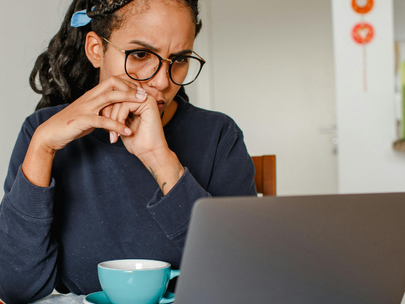 Woman sits at a laptop, thinking 
