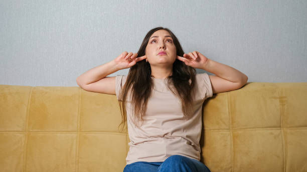 Woman blocking ears on couch due to noise, relating to Tauranga noise complaint rules.
