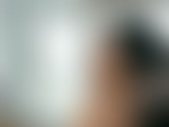 Gros plan de profil d'une femme aux cheveux bouclés et mouillés dans une douche minimaliste, utilisant une brosse ventilée pour répartir un soin capillaire. Elle affiche une expression sereine et naturelle avec très peu de mousse visible dans ses boucles bien définies.