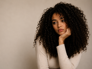 Jeune femme aux cheveux bouclés naturels dans une ambiance douce et minimaliste illustrant l’évolution du regard porté sur les cheveux texturés.