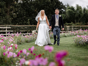 Bride and groom walk down a wild flower pathway at their marquee wedding