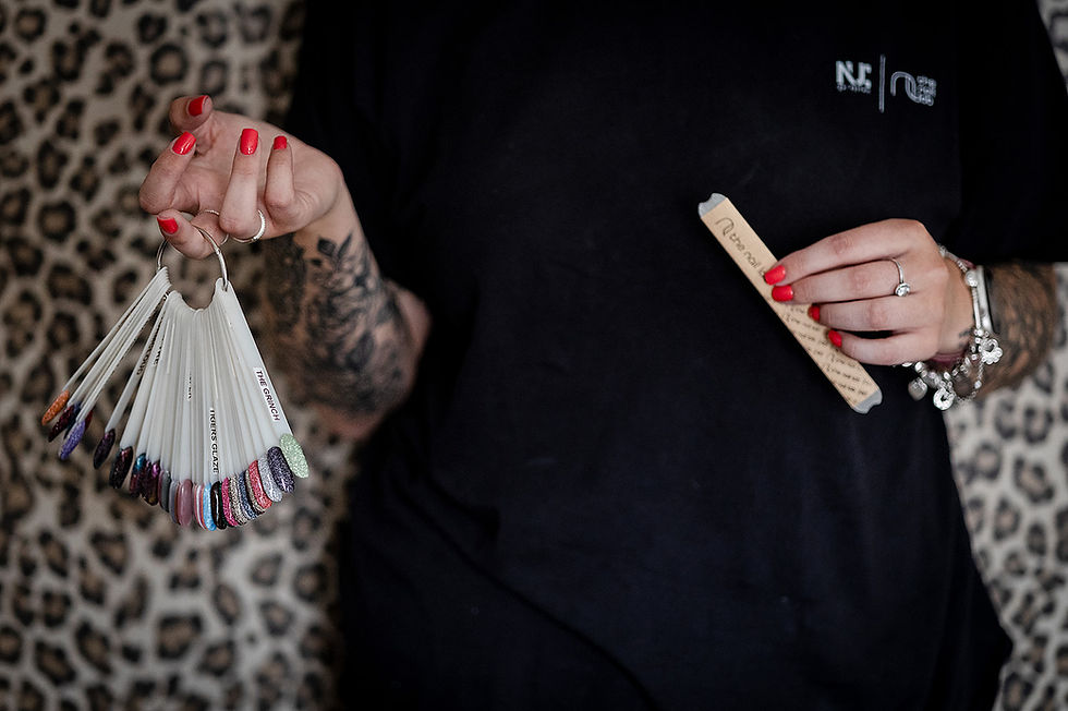 Tattooed hands with red nails hold a fan of glitter nail swatches and a nail file .