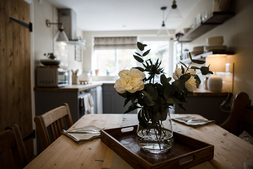 Vase of white flowers on a wooden table with napkins. Bright kitchen in the background with gray cabinets and natural light. Cozy mood.