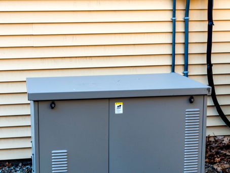 A standby home generator installed outside on a concrete pad, connected to the house with an electrical transfer switch.