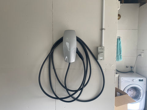 Tesla EV charger with coiled cable on a white wall