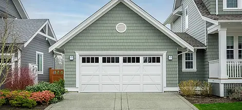 Traditional green craftsman-style home with a white garage door featuring decorative panel designs and upper glass windows, landscaped front yard, and a clean concrete driveway.