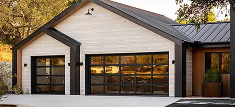 Modern contemporary home with full-view black glass garage doors, white brick exterior, black metal roof, wood accents, and a clean concrete driveway surrounded by mature trees.