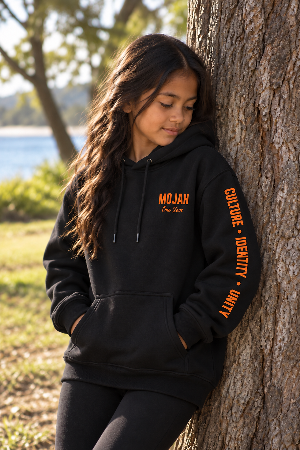 Girl in black HONU kids hoodie leaning against a tree.