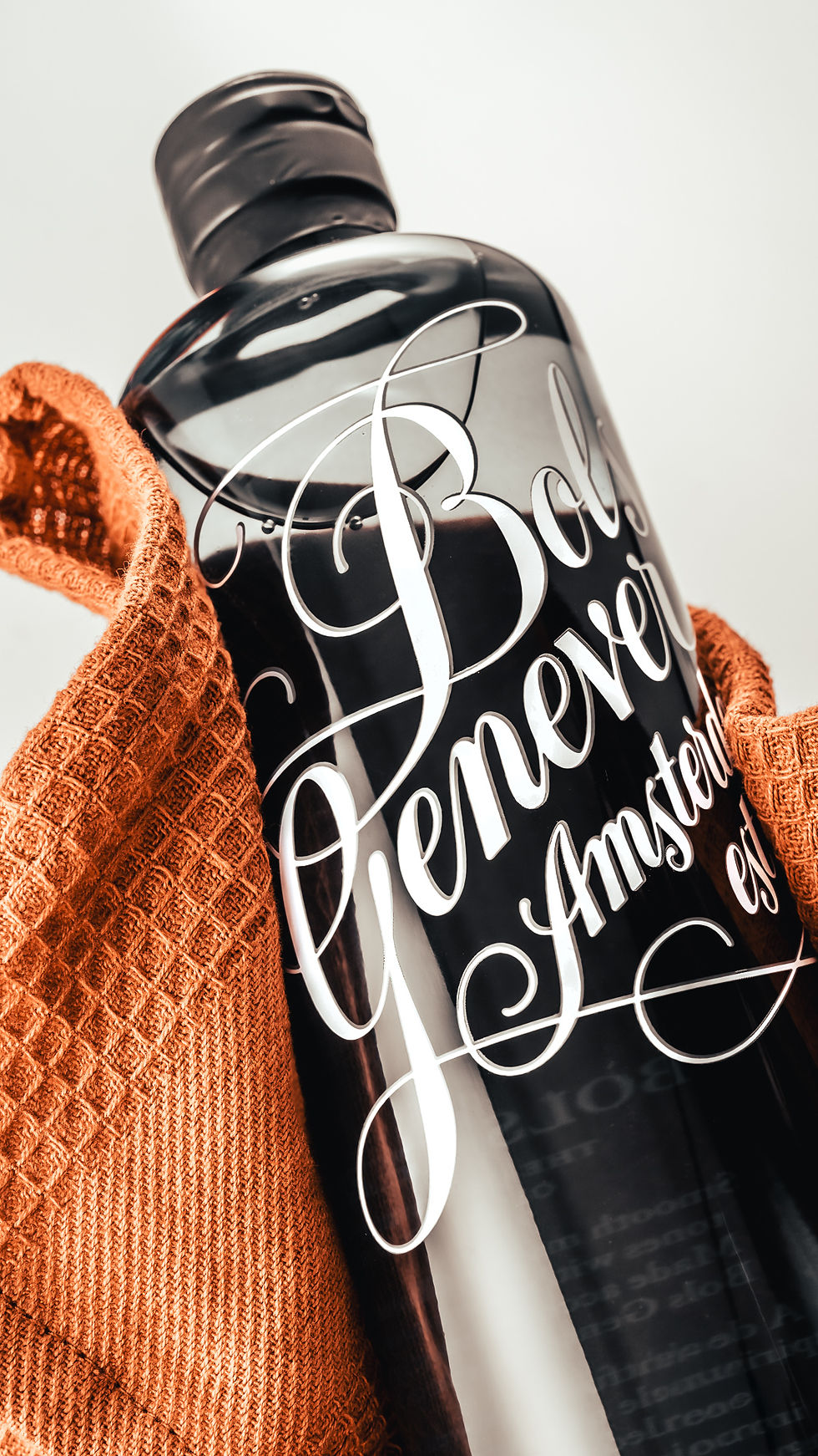 Bouteille noire de boisson marquée Beverly, enveloppée d’un pull orange, sur fond blanc.