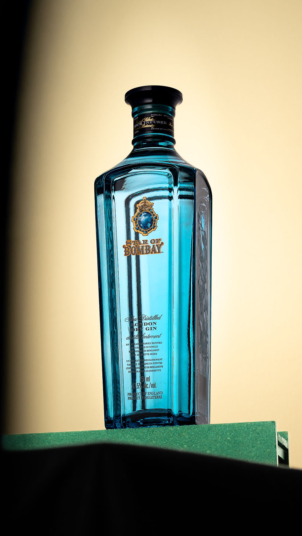 Bouteille bleue de gin Star of Bombay sur un socle vert, fond beige, étiquette visible.