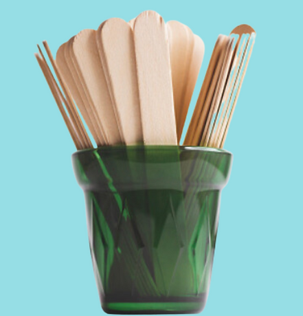 A green pot hold a bunch of wooden spatulas. The background is light blue