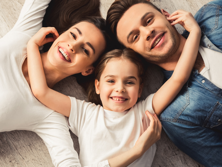 Parents and young daughter relaxing and playing on the floor, symbolizing a safe and nurturing home environment for hiring a nanny.