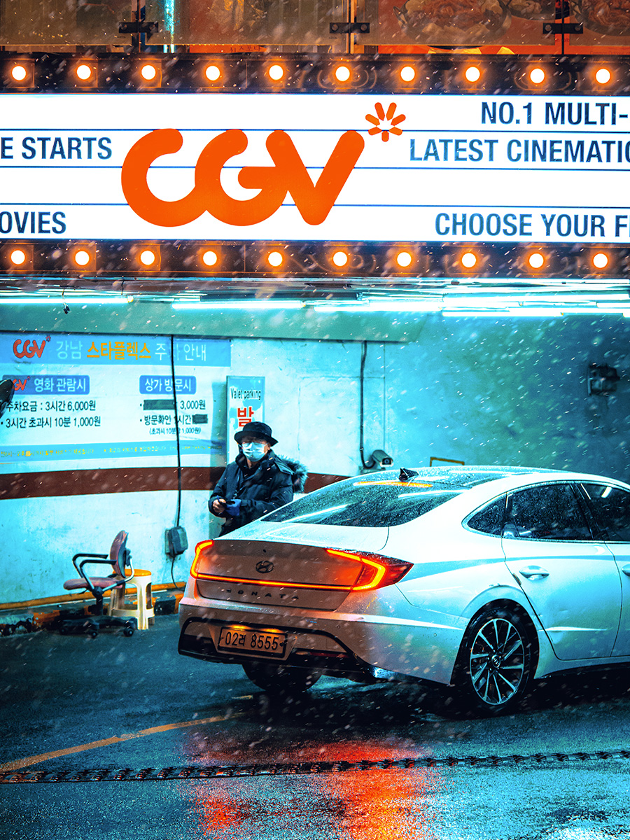 A man stepping around a Hyundai car underneath a neon sign.