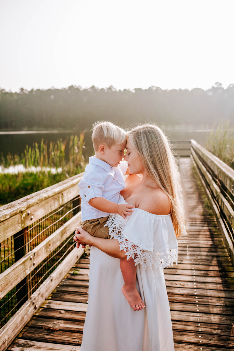 mother holds toddler son as they touch heads during morning maternity pictures