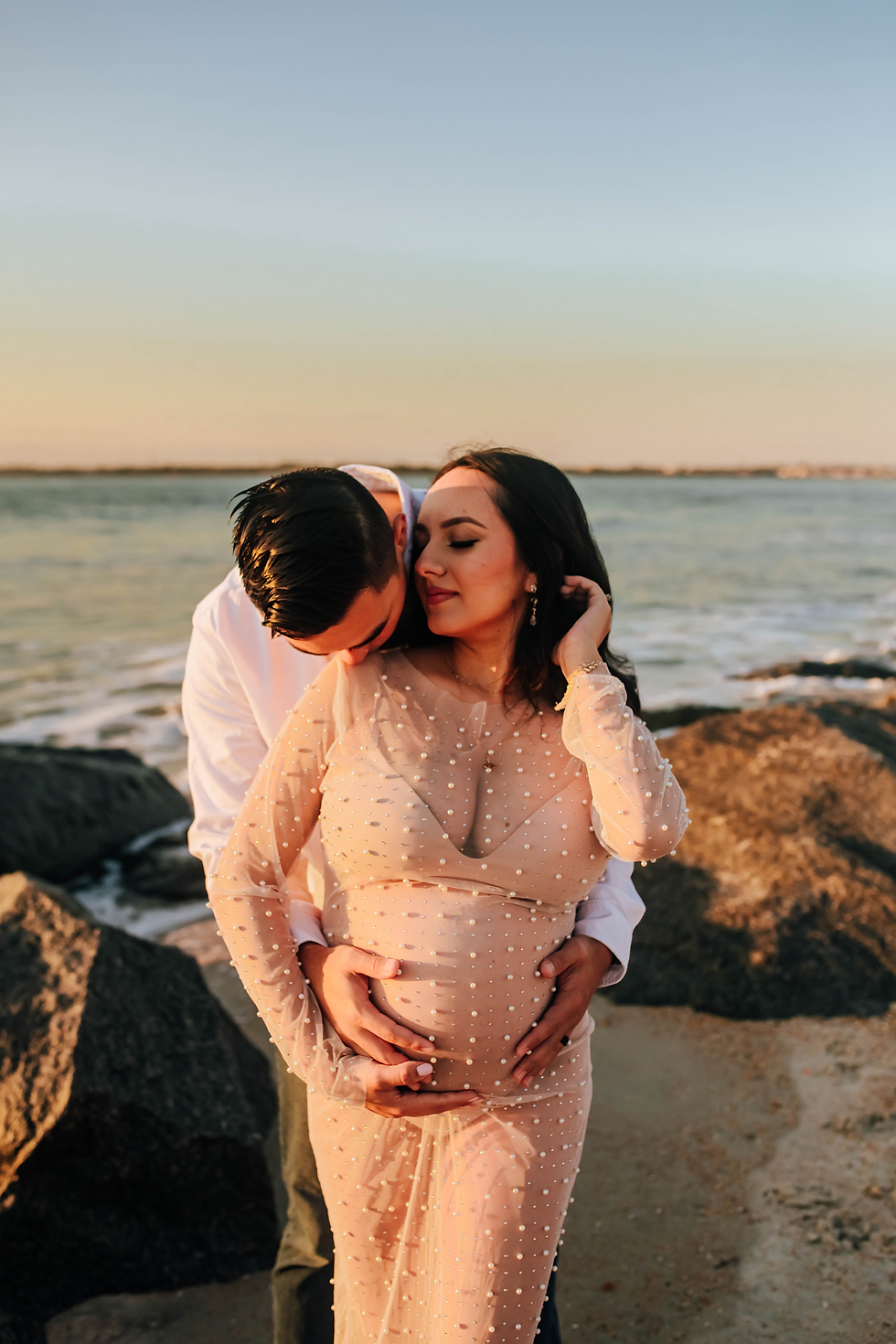 husband kissing expectant wife's shoulder during beach maternity shoot