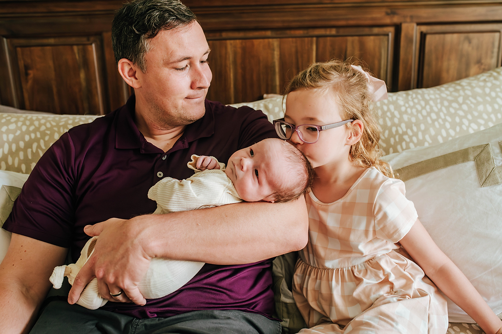 new dad holds newborn baby boy as 5 year old daughter leans in to give her brother a kiss during a newborn photography session