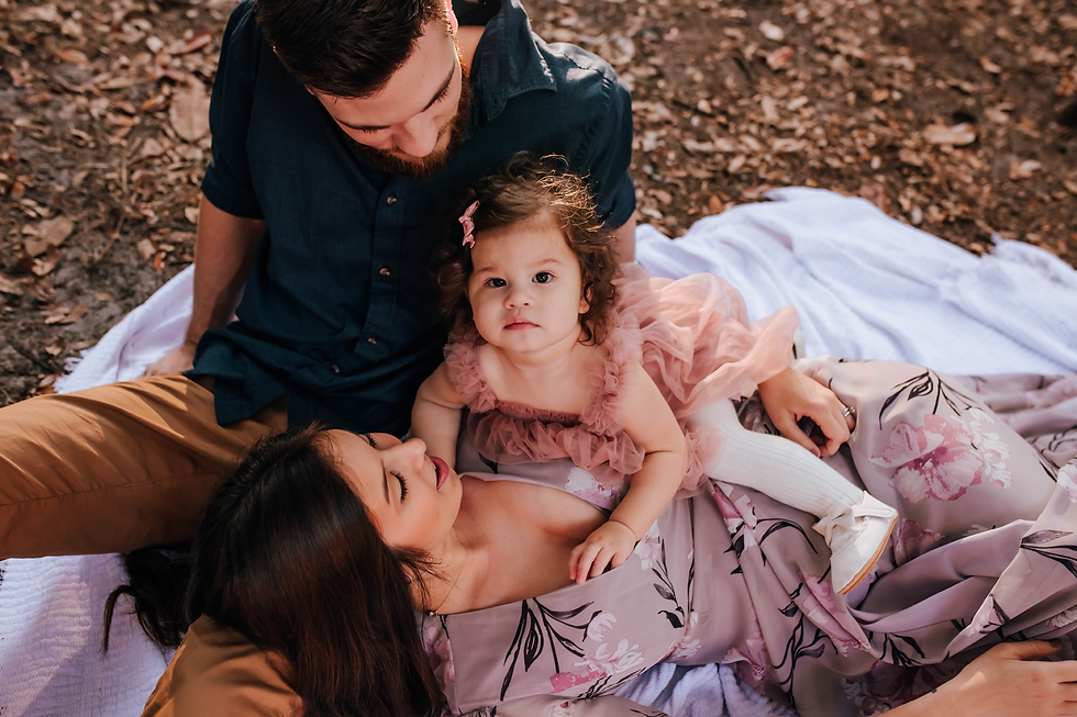 family cuddling together on blanket while little girl looks at photographer