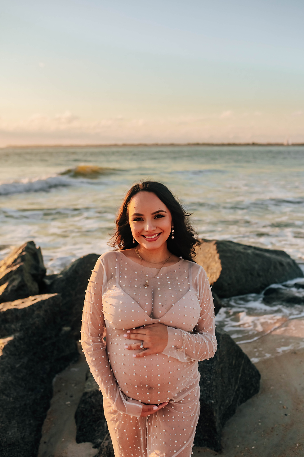 maternity photo of expectant mom smiling at camera on rocky beach at sunrise