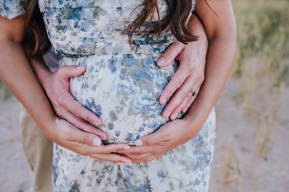 Hands gently cradle a pregnant belly in a floral dress in an outdoor setting, creating a serene and loving mood.