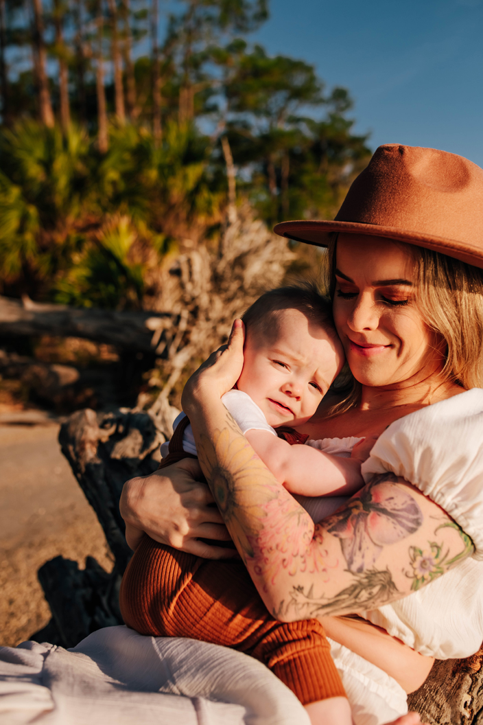 mother cuddling baby boy on driftwood tree during photoshoot
