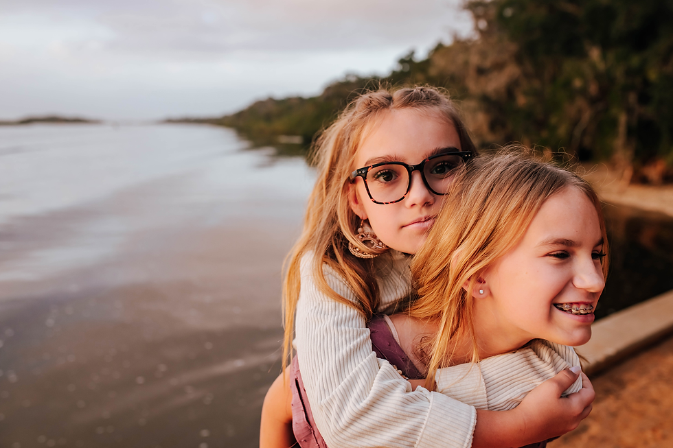 younger sister straight faced while piggy backing older sister during family photos