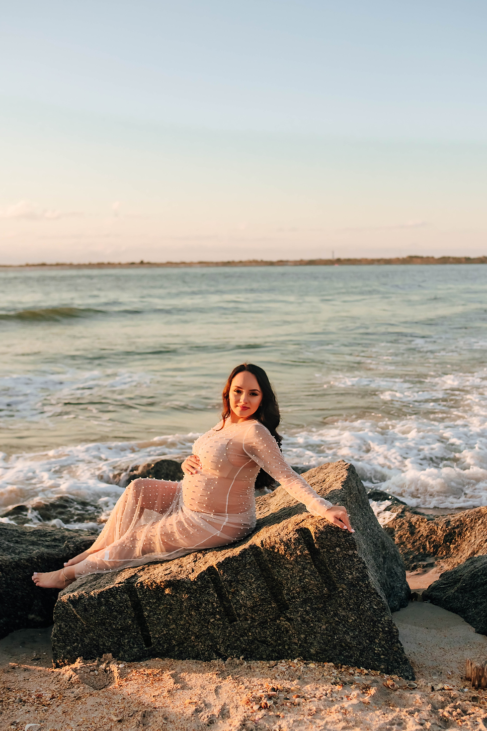 maternity picture of mother sitting on rock on beach at sunrise