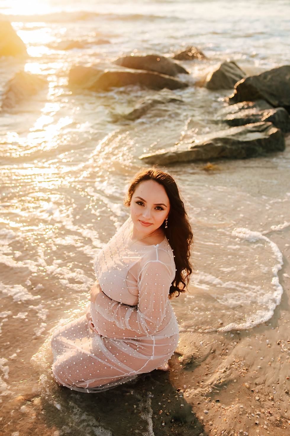 expecting mother in tide as water surrounds her knees during sunrise maternity photoshoot