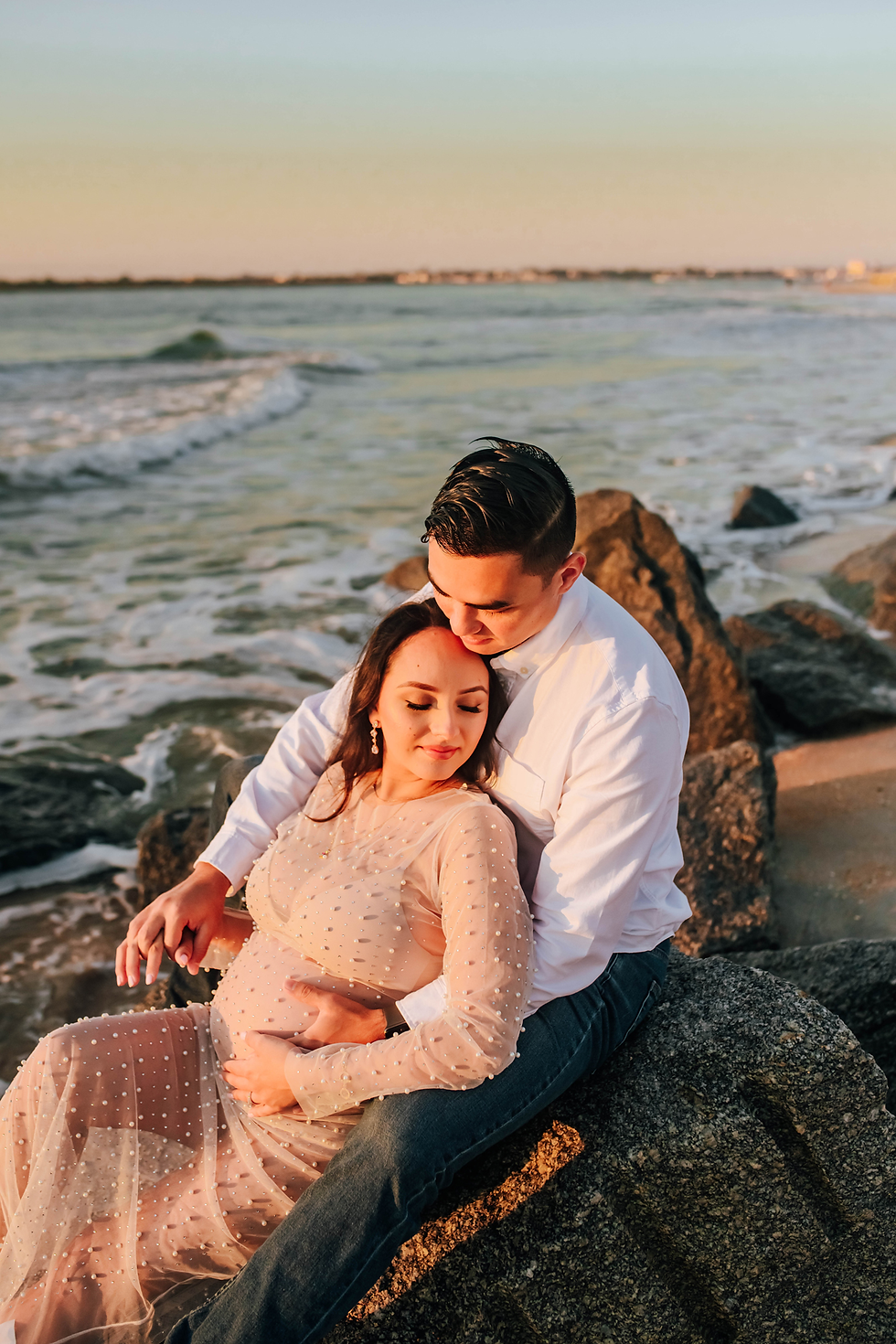 couple together on rocky beach with sun shining on them for sunrise beach photoshoot