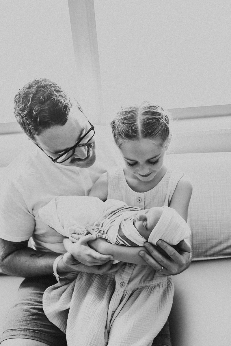 new father helps big sister hold her baby sister in a black and white portrait
