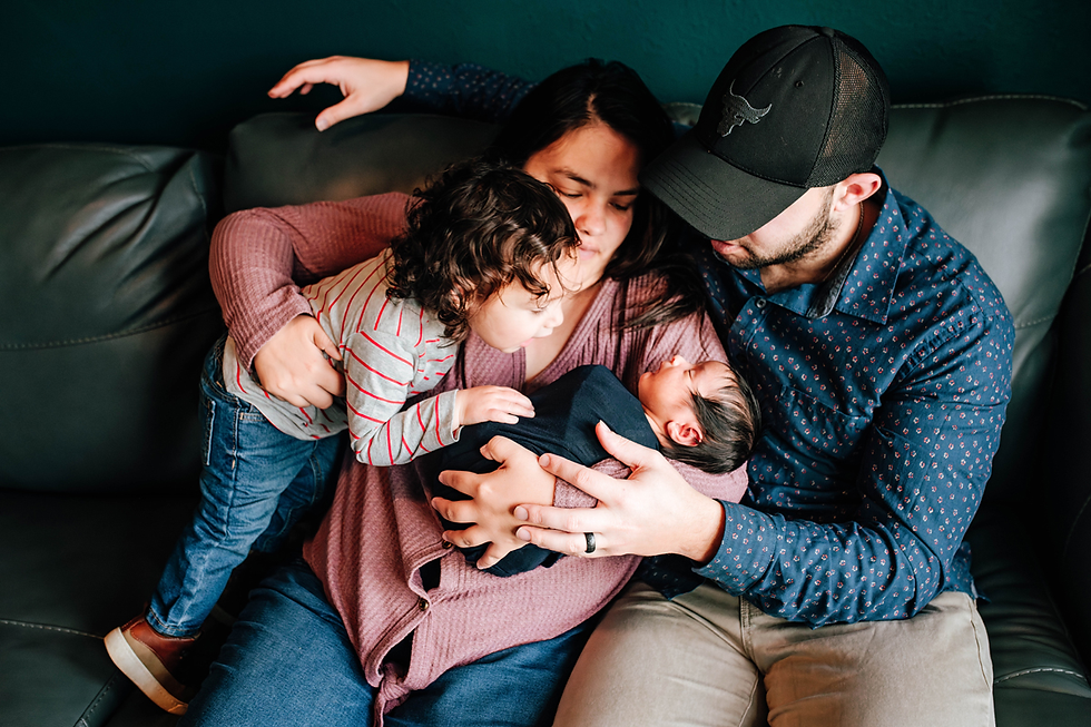 mother holds newborn baby boy as dad sits close and toddler brother leans in for a closer look