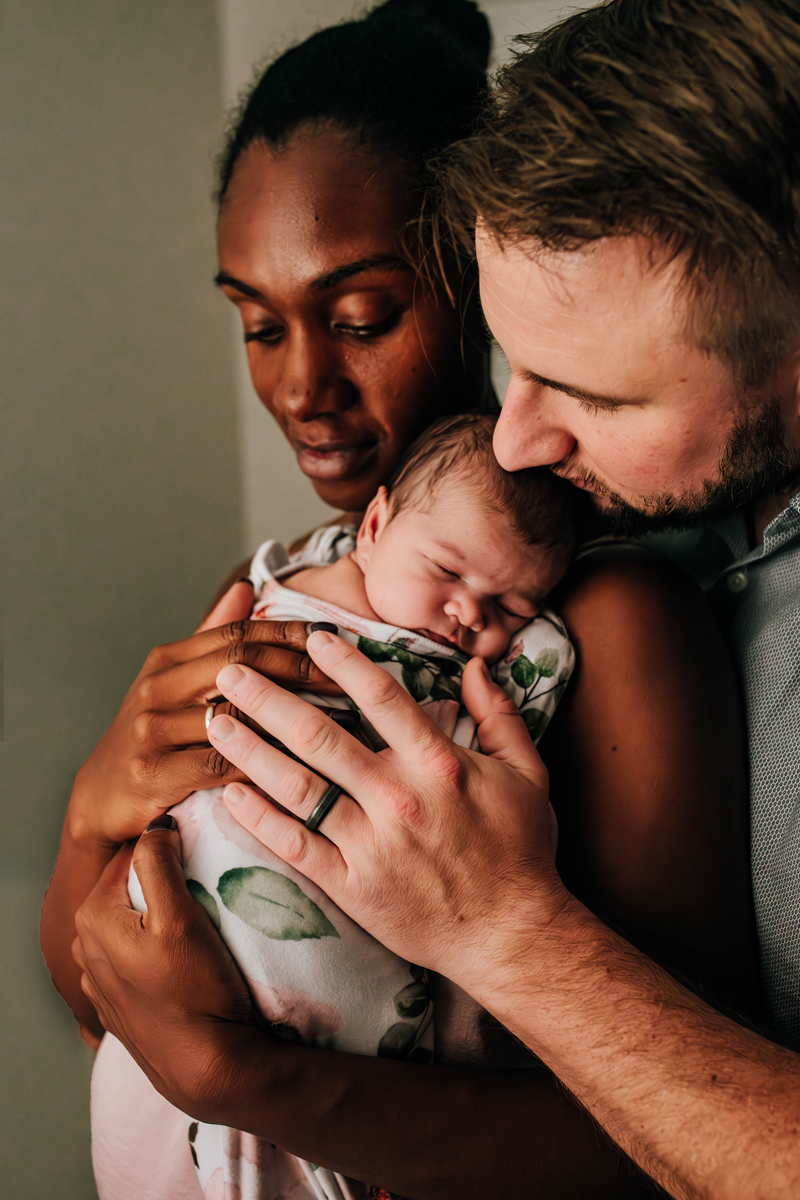 mother cuddle baby girl while dad gives the newborn girl a kiss