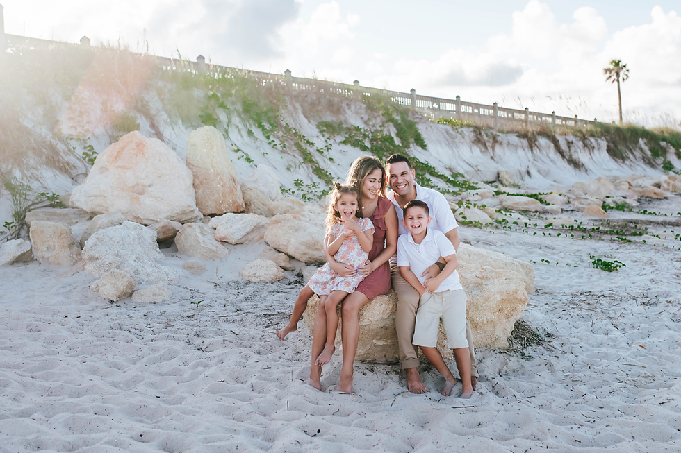 family sitting on large rock on beach laughing together