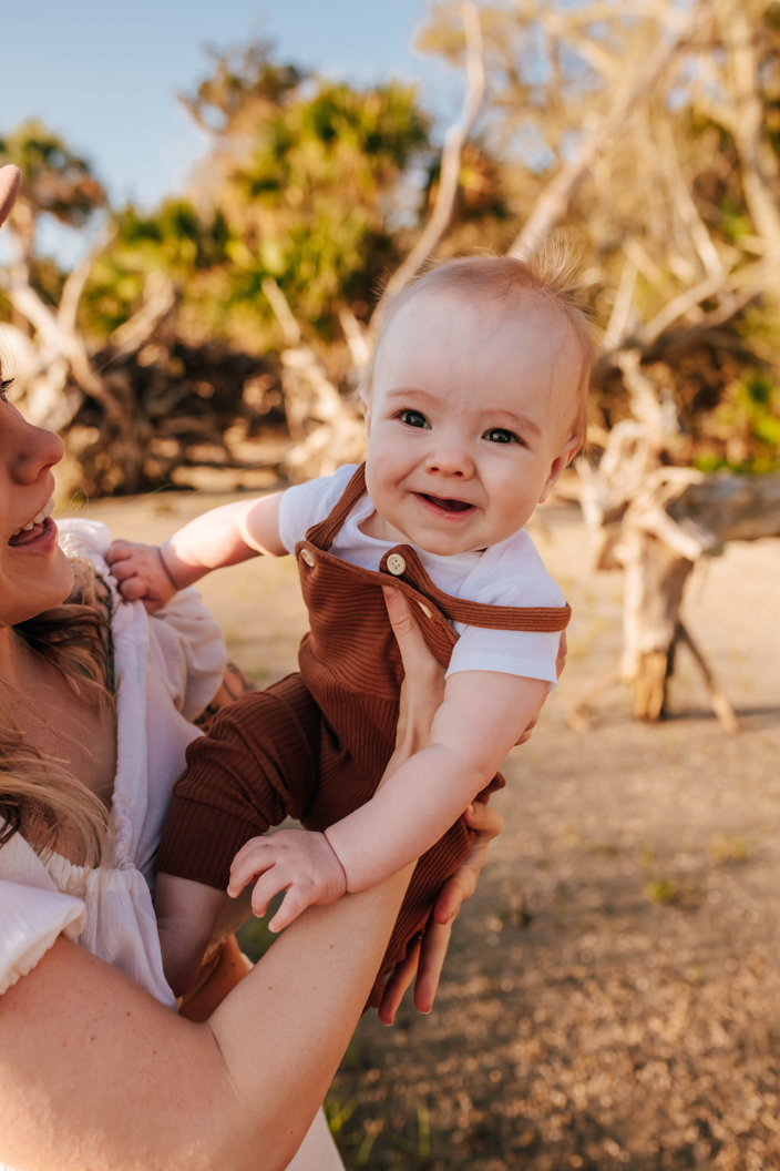 happy baby boy in overalls held by mom during family photoshoot