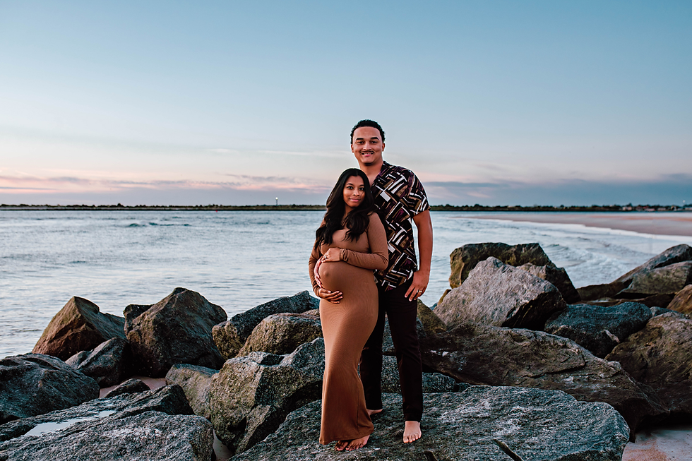 expecting couple stands on rocky beach posing for sunrise beach maternity pictures