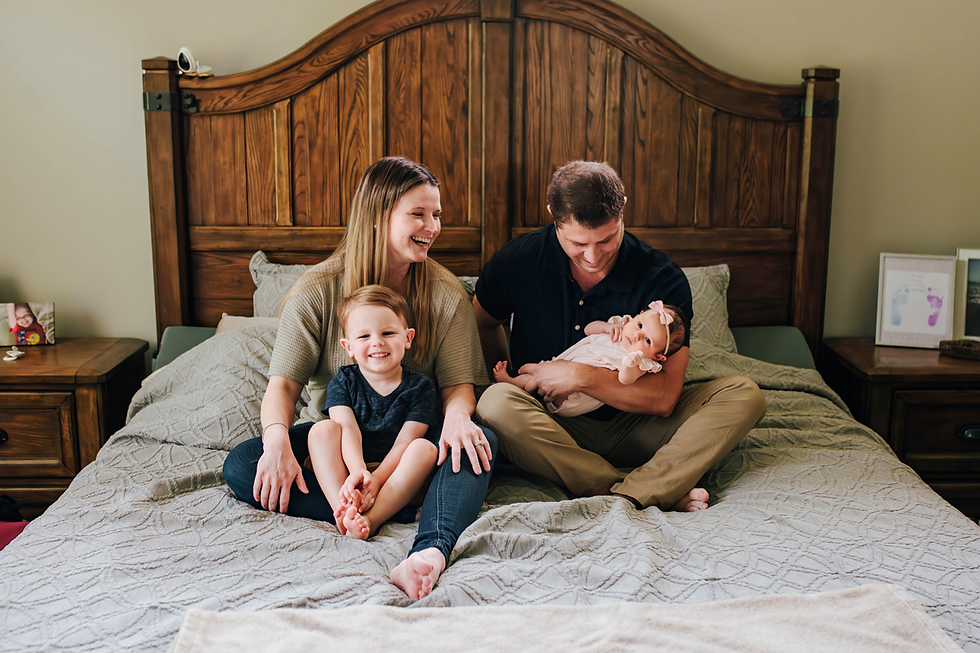 parents laughing as toddler and baby look at newborn photographer