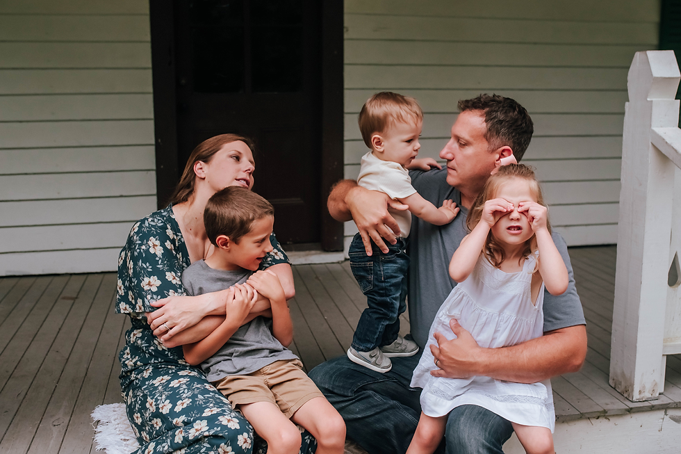 family together on front porch steps during family photos with daughter being silly and covering eyes