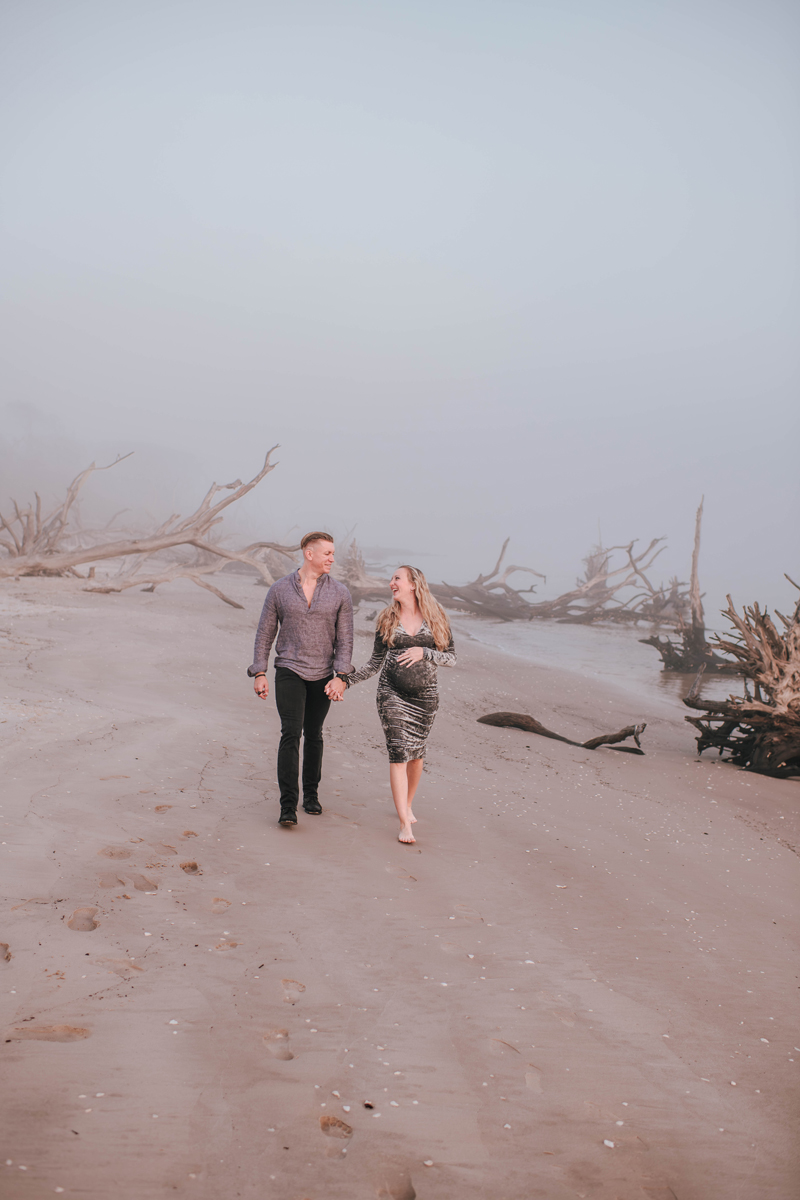 A couple walks hand in hand on a misty beach, surrounded by driftwood. The mood is serene and romantic.