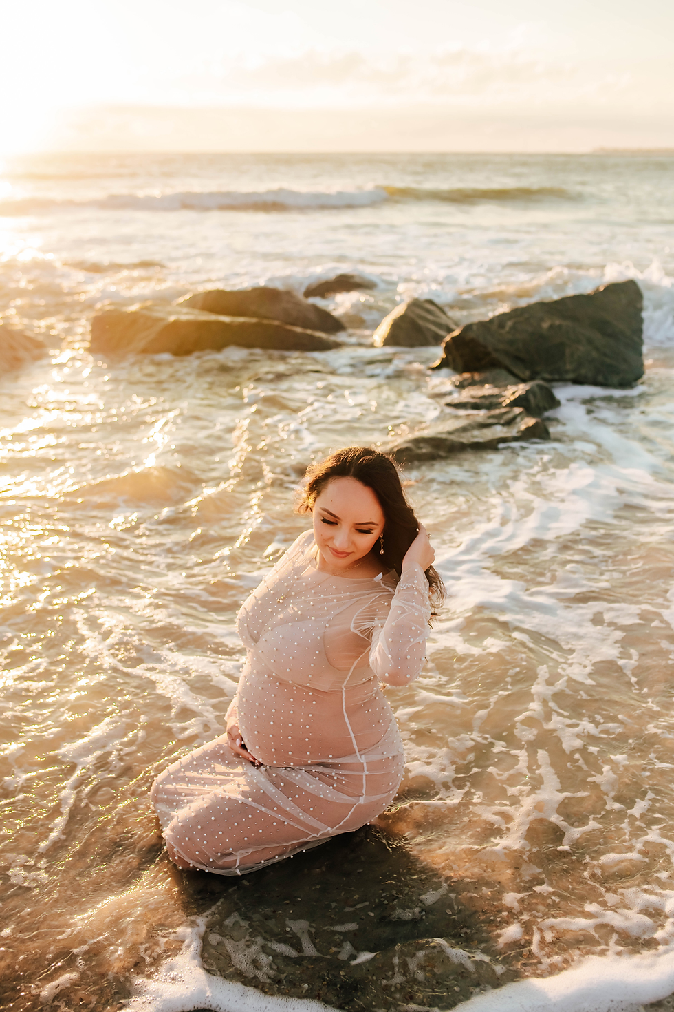 sunrise beach maternity photography session of mother in water break of ocean