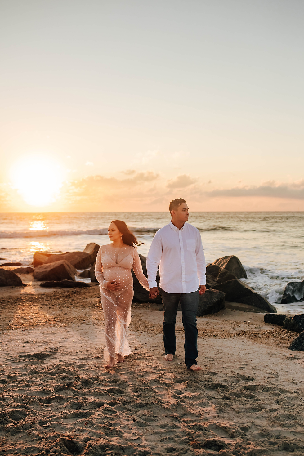 couple walking on beach hand in hand during sunrise maternity photography session