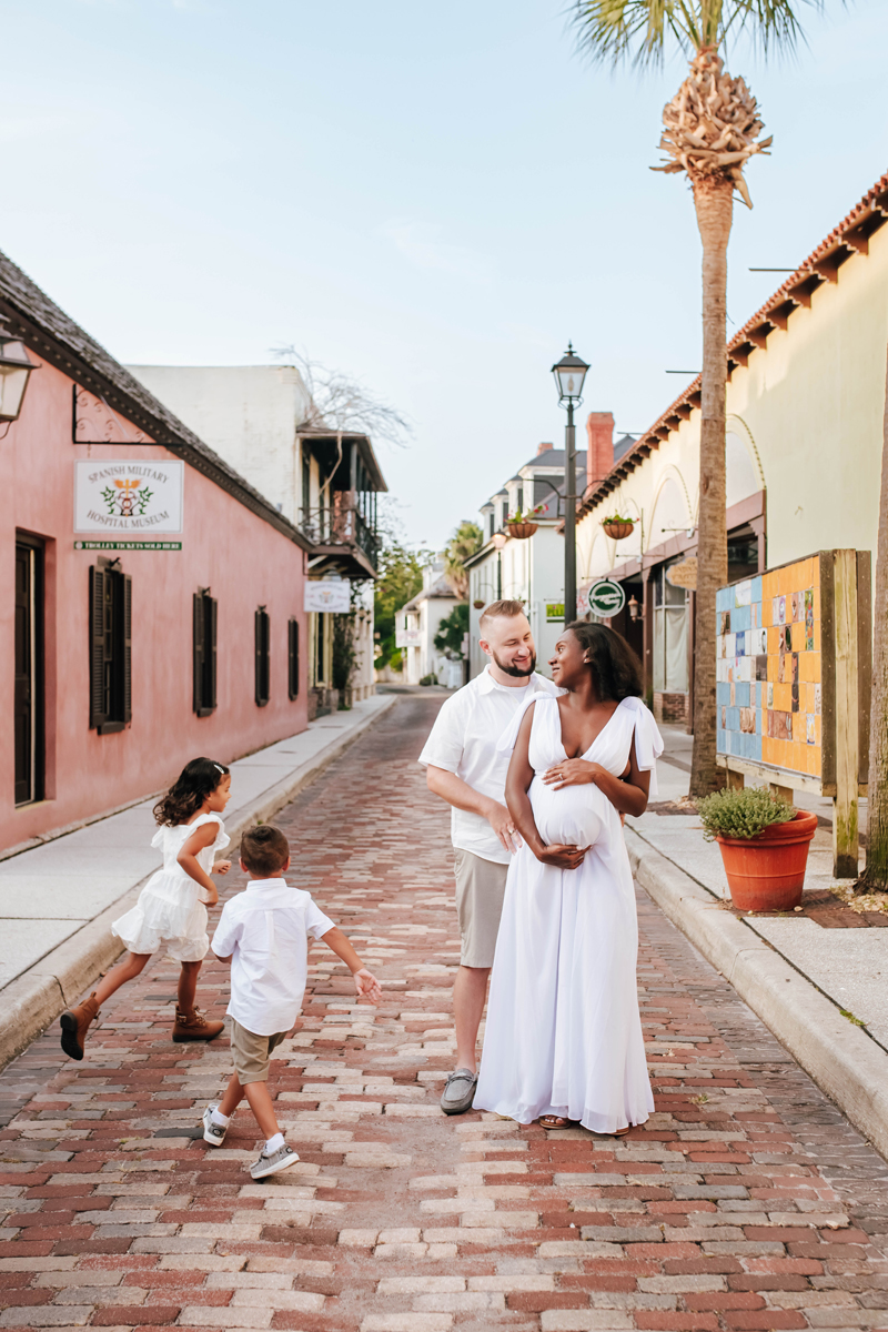 brother and sister run around expecting parents on historic brick roadway during maternity photos